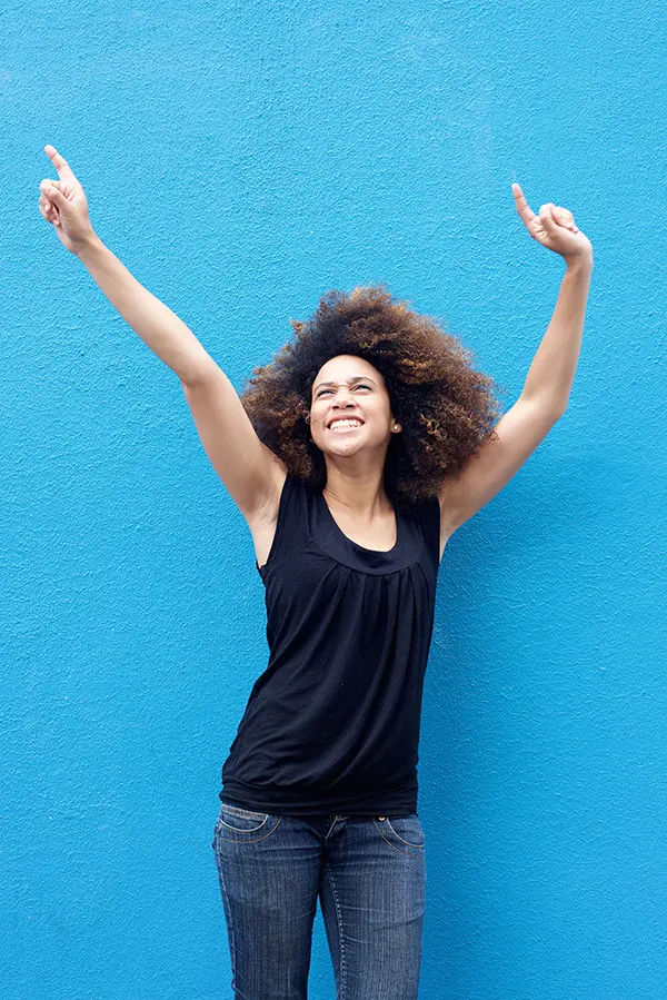 PMS-Treatment A woman in a dark blue tank top standing in front of a bright blue wall, raising her arms in celebration of relief from PMS from Richard Conlen, MD, FACOG in Boca Raton.