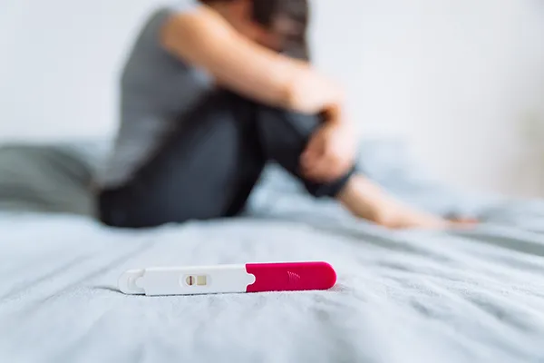 infertility-treatment A negative pregnancy test on a bed with a sad woman in the background. Get infertility treatment from Richard Conlen, MD, FACOG in Boca Raton.